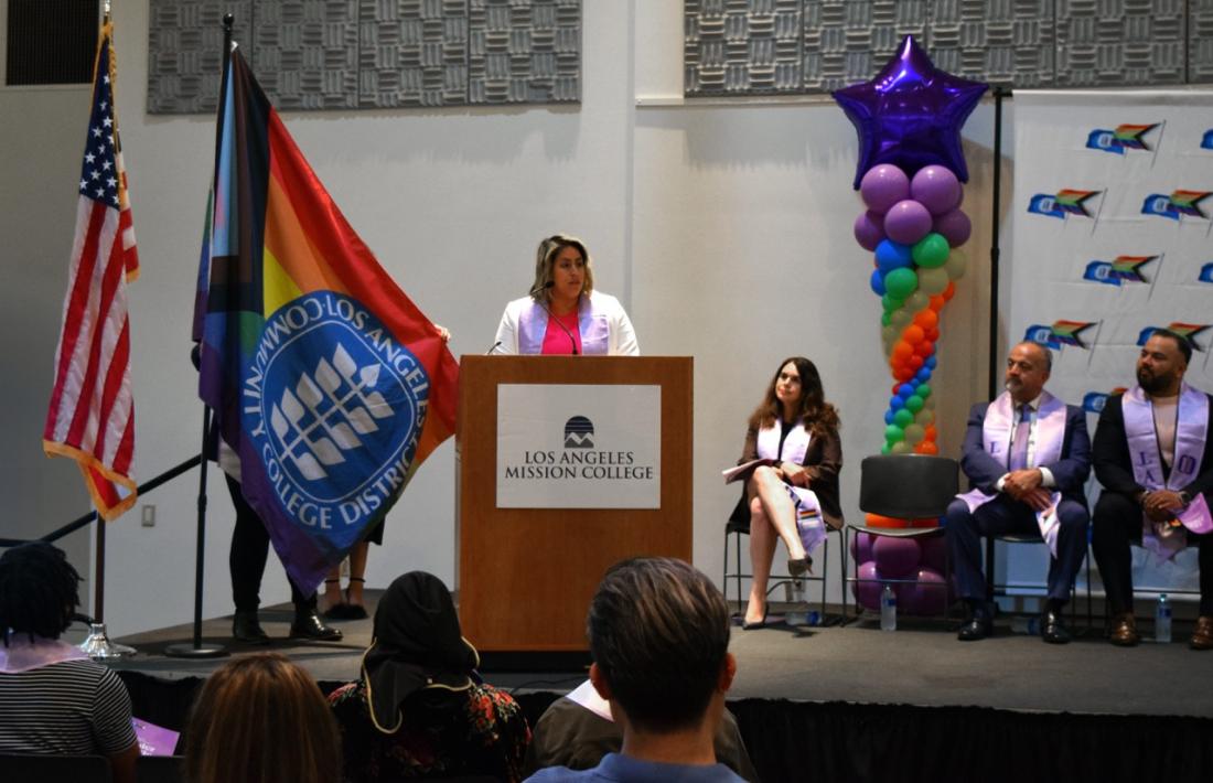 CA State Senator Caroline Menjivar speaking at the 2024 Lavender Graduate Ceremony next to the LGBTQI+ flag.